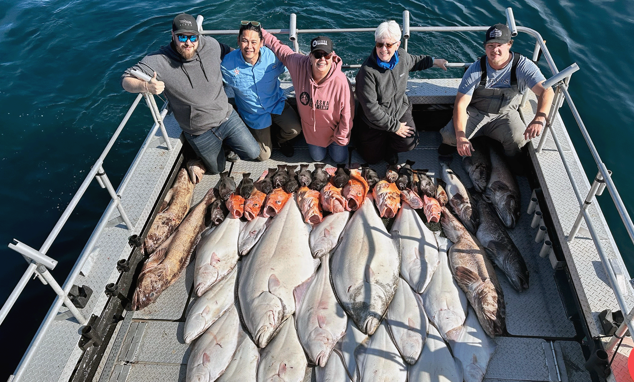 A group of anglers proudly displaying their impressive catch of Halibut, Rockfish, and other saltwater species aboard a fishing boat in Seward, Alaska.